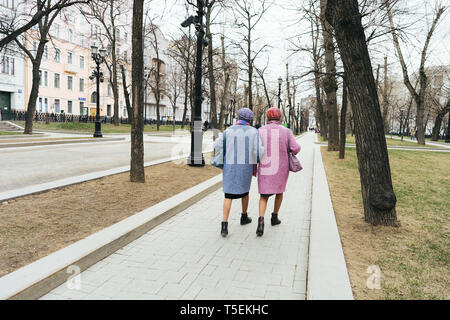 Moscow, Russia - 04 20 2019: Two elegant older grandmothers identically dressed in a pink and blue coat and similar hats walk along the boulevard of a Stock Photo