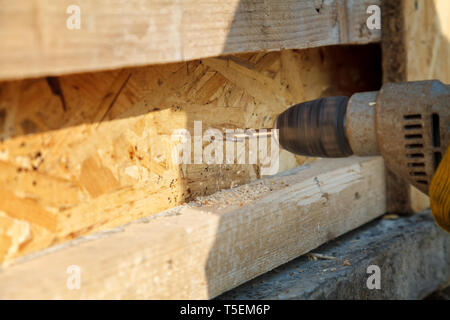 Drilling wooden beams electric drill. Worker makes a hole in the pine rail Stock Photo