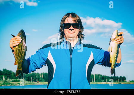 Happy fisherman showing caught fish. Caucasian man holds two fish. Angler on river fishing Stock Photo