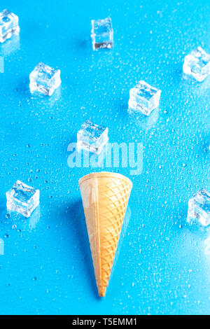 Empty ice cream cone and ice cubes on blue background Stock Photo