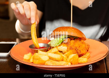 Woman eating burger with hand dipping french fried to ketchup. Stock Photo