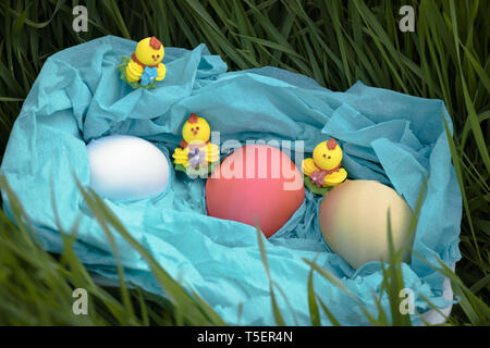 Three toy chickens and three easter eggs on the grass in a blue basket Stock Photo