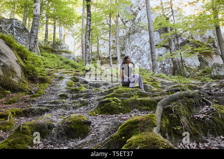 Young attractive girl sit on the big rock in forest