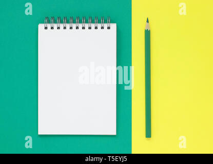 Open blank notepad with a green pencil, on a green and yellow flat lay background. With copy space. Stock Photo