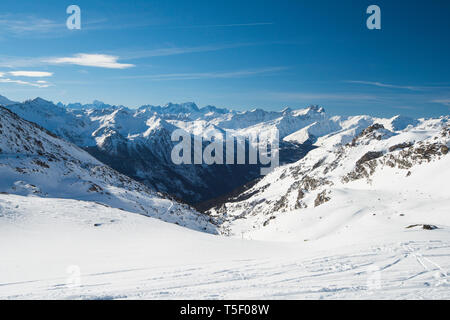 Panoramic view down snow covered valley in alpine mountain range on blue sky background Stock Photo