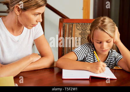Girl doing homework under control on mother Stock Photo