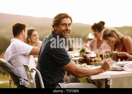 Handsome man having drinks with friends sitting by at dinner party. Young guy enjoying at outdoor party with friends.