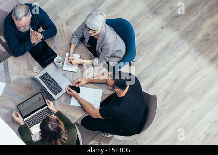 Business team sitting around a table and talking over new ideas. High angle view of corporate professional having a meeting in office. Stock Photo