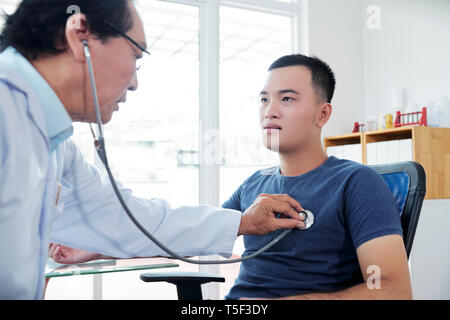 Doctor checking heartbeat of young man Stock Photo
