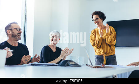 Businesspeople clapping hands after successful brainstorming session in boardroom. Group of men and women applauding after productive meeting. Stock Photo