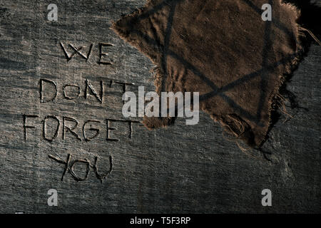 high angle view of a ragged jewish badge on a gray rustic wooden surface with the text we dont forget you carved in it Stock Photo