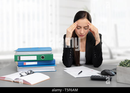 Tired businesswoman in the office. Young female employee unhappy with excessive work. Stock Photo