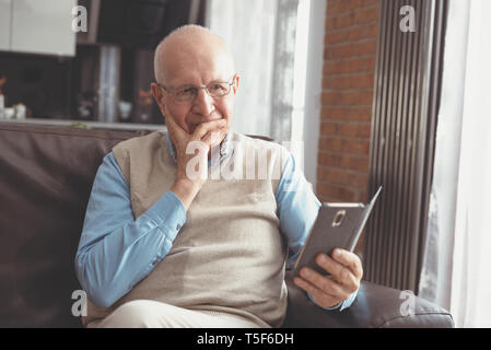 Senior man using a smartphone and smiling while sitting on couch at home. Stock Photo