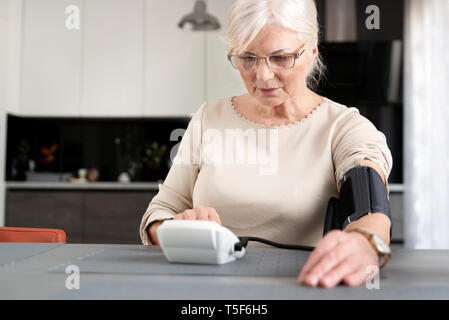 Senior adult woman measuring blood pressure at home Stock Photo