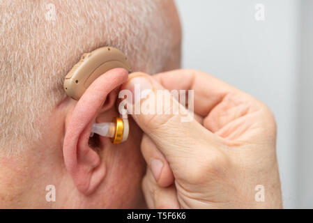 Hearing aid in the ear of aged old man. Senior using modern hearing aid Stock Photo