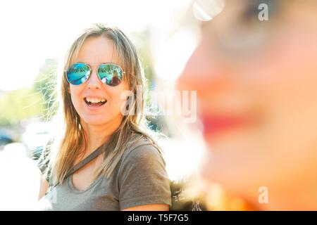 Woman in green T-shirt smiling in background second woman in out of focus foreground. Stock Photo