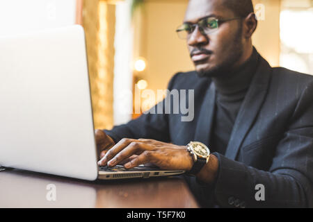 Young handsome dark-skinned businessman in a cafe working behind a laptop with a cup of tea. Stock Photo