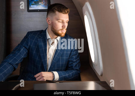 attractive and successful businessman in an expensive suit working sitting in the chair of his private jet. Stock Photo