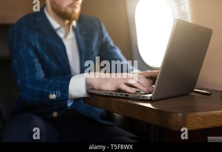 Attractive and successful businessman working on a laptop while sitting in a chair of his private jet. Stock Photo
