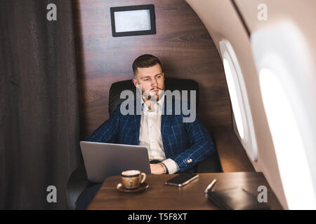Attractive and successful businessman working on a laptop while sitting in a chair of his private jet. Stock Photo