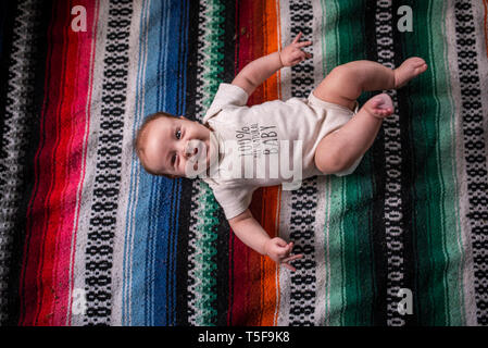 Three month old baby boy smiles big laying on colorful blanket Stock Photo