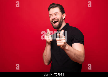 Hey you. Bearded man smiling and pointing at camera over red background Stock Photo
