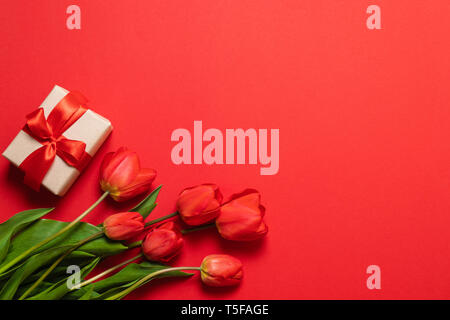 Bunch of red tulips and gift boxes with red ribbons on a red background. Stock Photo