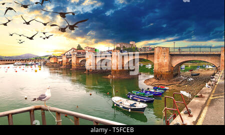 Idyllic and stunning coastal town in Spain. Bridge over the sea and sunset seascape. Boats in the harbor.San Vicente de la Barquera.Cantabria. Stock Photo