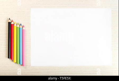 Colourful crayons and white sheet of paper on white plank background Stock Photo