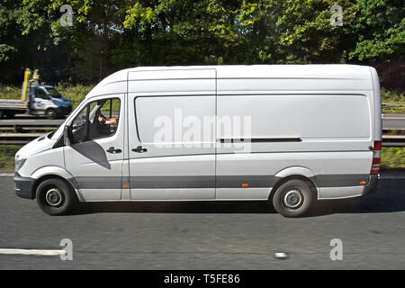 Side view of  white light commercial cargo van & driver driving along dual carriageway motorway road in lane three beside crash barrier England UK Stock Photo