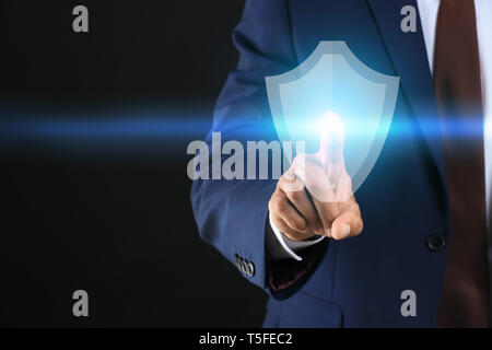 Businessman pressing shield icon on dark background. Data security concept Stock Photo