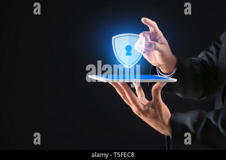 Businessman with tablet PC and shield icon on dark background. Data security concept Stock Photo