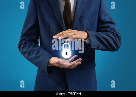 Businessman with glowing padlock icon on blue background. Data security concept Stock Photo