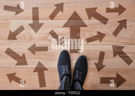 Man standing on wooden floor with arrows pointing in different directions. Concept of choice Stock Photo