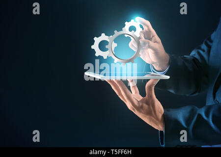 Businessman with tablet PC and digital gearwheels on dark background. Concept of Internet and technical support service Stock Photo