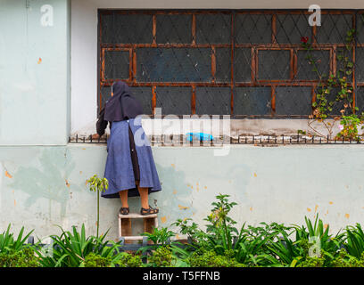 Catholic nun with habit cleaning the outside part of a convent in the city center of Cuenca, Ecuador. Stock Photo