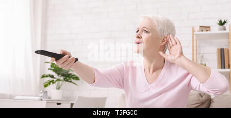 Elderly woman rising tv set volume with remote control Stock Photo