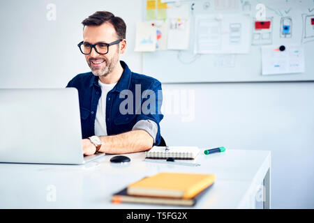 Casual businessman working on laptop at desk in office Stock Photo