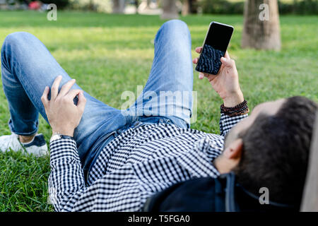 Man lying on meadow in city park using smartphone Stock Photo