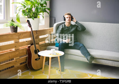 Relaxed young man with tablet and guitar listening to music with headphones Stock Photo