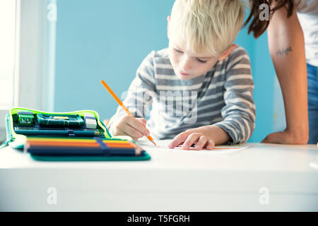 Boy doing homework with mother leaning on desk Stock Photo