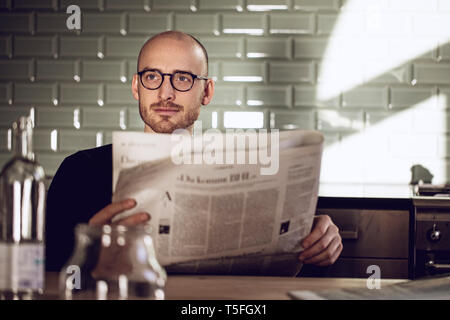 Man sitting in kitchen, reading newspaper Stock Photo