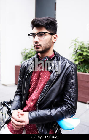 Portrait of handsome man in leather jacket and glasses with headphones,  leaning on fixie Stock Photo