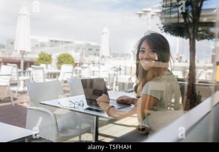 Portrait of smiling woman sitting at pavement cafe working on laptop Stock Photo