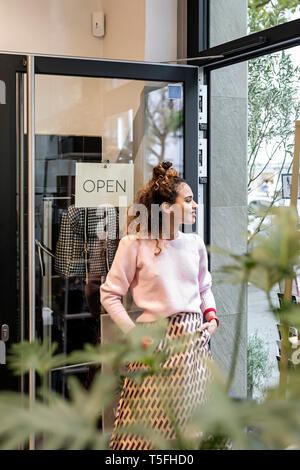 Young woman standing in open shop door, smiling Stock Photo