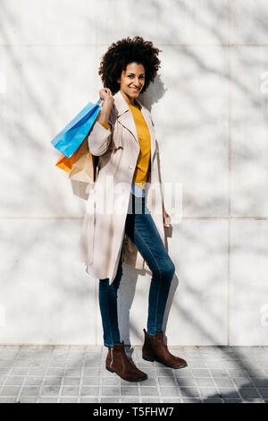Portrait of smiling woman with shopping bags standing at a wall Stock Photo