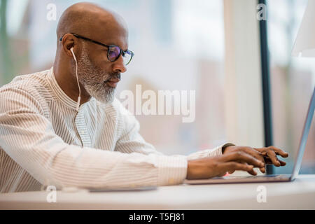 Mature businessman with earphones working on laptop Stock Photo
