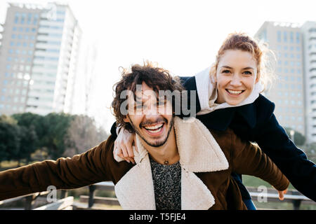 Happy couple enjoying a piggyback ride in a sunny city park, playful ...