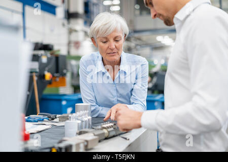 Businessman and senior businesswoman examining workpiece in a factory Stock Photo