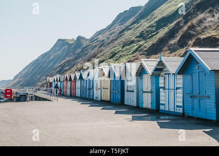 Sheringham, UK - April 21, 2019: People walking by colourful beach huts by the sea in Sheringham on a sunny day. Sheringham is an English seaside town Stock Photo